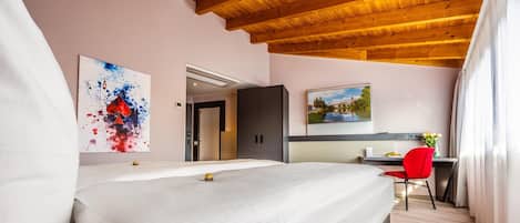 A hotel room with a bed, a desk, a chair, and artwork on the walls.