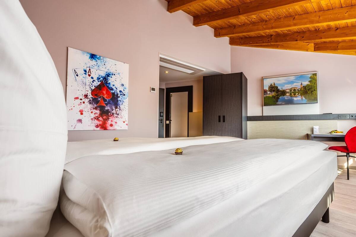 A hotel room with a bed, a desk, a chair, a painting, and a window.