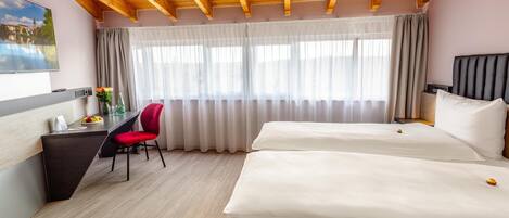 A hotel room with a wooden ceiling, a desk with a chair, a bed, and a large window with curtains.
