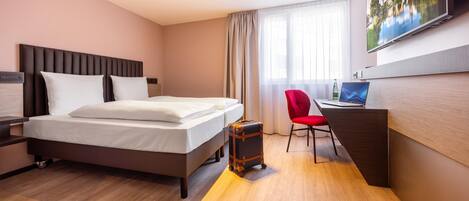 Una habitación de hotel con una cama, un escritorio con una computadora portátil, una silla y una maleta.