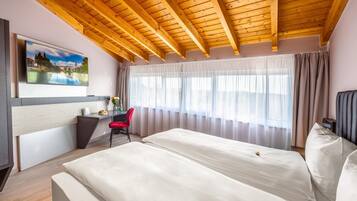 Ein Hotelzimmer mit Holzboden, einem Bett, einem Schreibtisch mit Stuhl, einem Fernseher und einem Fenster mit Vorhängen.