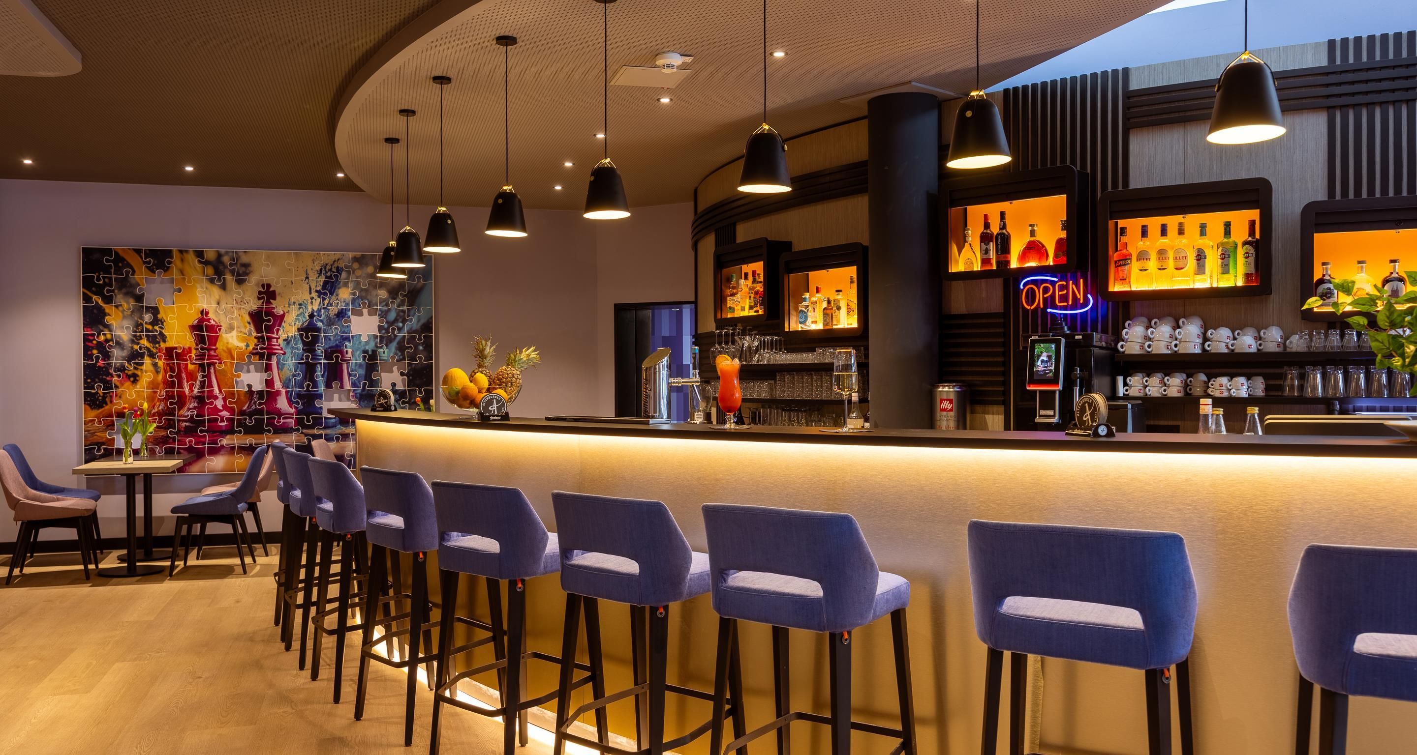 Una zona de bar con mostrador, taburetes y una variedad de botellas y vasos.