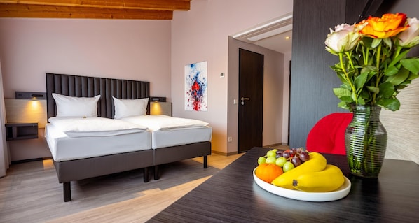 A hotel room with a double bed, bedside tables, a wall art piece, a door, and a table with fruit. - Best Western Hotel Altenburger Land (Altenburg)