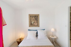 Une chambre à coucher avec un lit, une table de chevet avec une lampe, un tableau encadré au mur et un rideau sur le côté gauche.