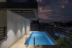A rooftop pool with a metal railing, a concrete wall, and a view of the city skyline at dusk. - Opulence Reality Stays (Lagos)
