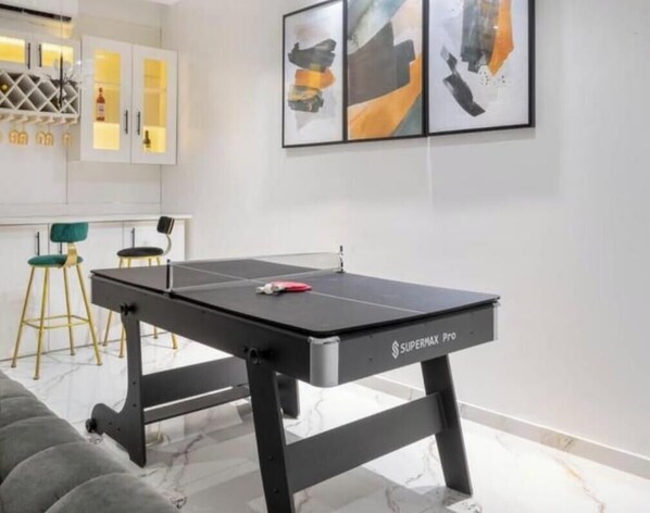 A room with a table tennis table, a sofa, a kitchen area, and abstract art on the wall. - Opulence Reality Stays (Lagos)