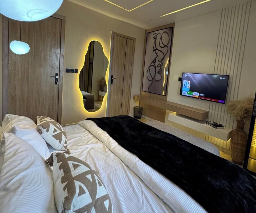 A modern bedroom with a bed, a TV, a mirror, and a wall-mounted shelf.