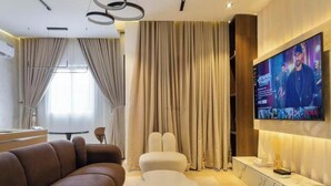 A modern living room with a sectional sofa, a white ottoman, a marble console table, and a flat-screen TV mounted on the wall. - Opulence Reality Stays (Lagos)