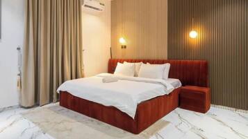 A modern bedroom with a large bed, a bedside table, a wall-mounted air conditioner, and a patterned floor.