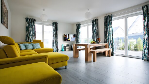 Un salon moderne avec un canapé jaune, une table à manger en bois et un téléviseur.