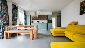 Un salon moderne avec un canapé jaune, une table à manger en bois et une cuisine en arrière-plan.
