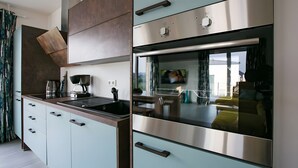 Une cuisine moderne équipée d’un four encastré, d’une machine à café et d’une grande fenêtre.