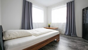 Une chambre à coucher avec un lit, une table de chevet, une plante en pot et une fenêtre avec des rideaux.