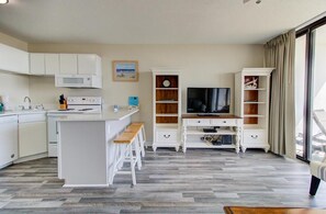 Een ruimtelijke leefruimte met een kitchenette, een televisie en een eethoek.