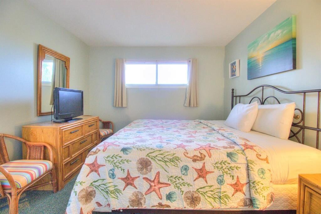Een slaapkamer met een bed, een televisie op een dressoir, een stoel en een raam.