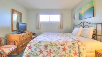 Een slaapkamer met een bed, een televisie op een dressoir, een stoel en een raam.