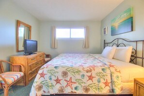 A bedroom with a bed, a television on a dresser, a chair, and a window. - Oceanfront 1 Bedroom Condo at Carolina Beach 0206 (Carolina Beach)