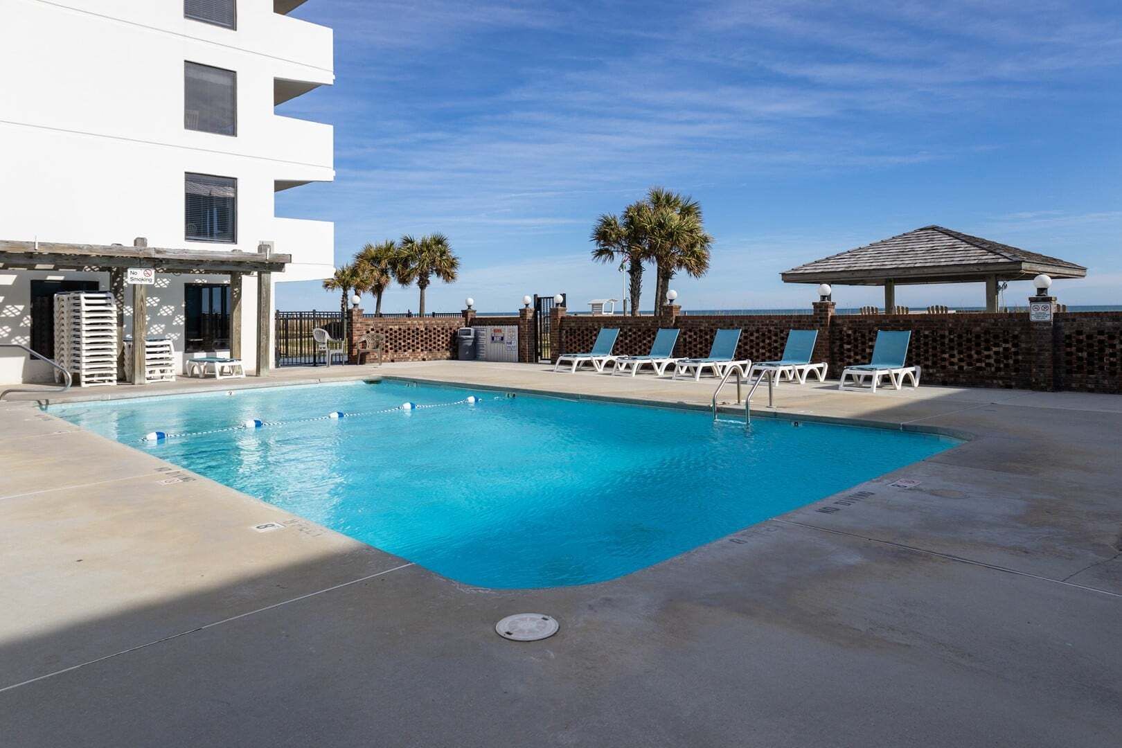 Une piscine avec des chaises longues, un mur de briques et un bâtiment doté de balcons.