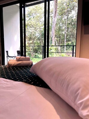 A bedroom with a bed, pillows, and a view of trees through large windows. - A Estadia tranquila con vista al bosque (Rionegro)