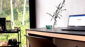 Un espacio de trabajo con una computadora portátil, una cafetera, un florero con planta y una botella de agua sobre una estantería.