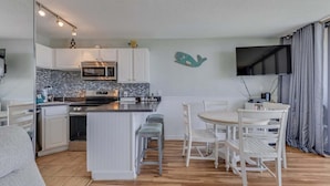 Et moderne køkken med hvide skabe, en mikrobølgeovn og et flisebeklædt bagpanel. Der er et spiseområde med et hvidt bord og stole.