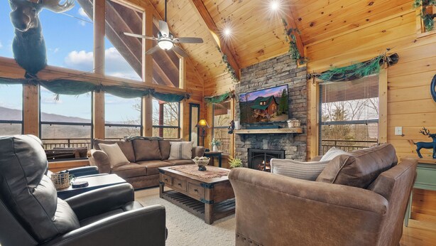 A cozy log cabin interior with a fireplace, leather sofas, a television, and a ceiling fan. - Luxury Views and Prime Smoky Mountain Location (Sevierville)