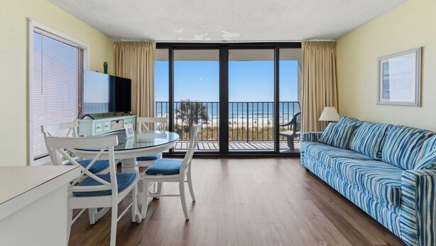 Ein Zimmer mit Balkon, einem Esstisch mit Stühlen, einer Couch und einem Fernseher.