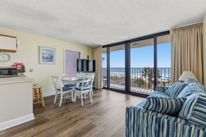 Et værelse med spiseplads, en sofa, et fjernsyn og en balkon med udsigt over stranden.