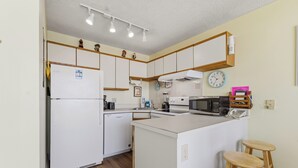 Eine kleine Küche mit Kühlschrank, Mikrowelle und Holz-Barhocker.