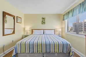 Hotelkamer met een bed, twee nachtkastjes, een raam met zonwering, een spiegel aan de muur en een lijst met een foto.