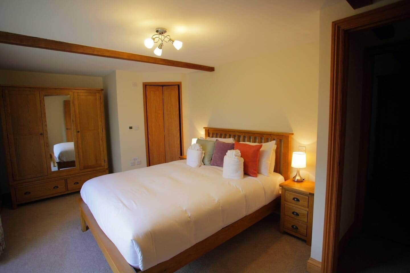 A bedroom with a bed, bedside table, lamp, wardrobe, and a mirror.