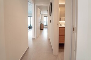 Een gang met een houten kast, een klok aan de muur en een deur naar de badkamer.