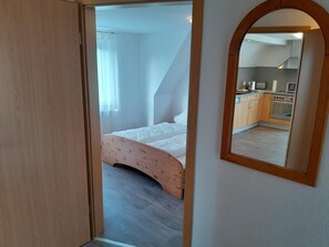 A bedroom with a curved headboard, a visible kitchen area with appliances, and a mirror reflecting the room. - NEW! "Nordseeluft" Vacation Rental (Dornum)