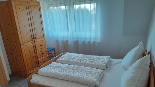 A wooden bed with two pillows and a mattress, a wooden wardrobe, and a chair. - NEW! "Nordseeluft" Vacation Rental (Dornum)