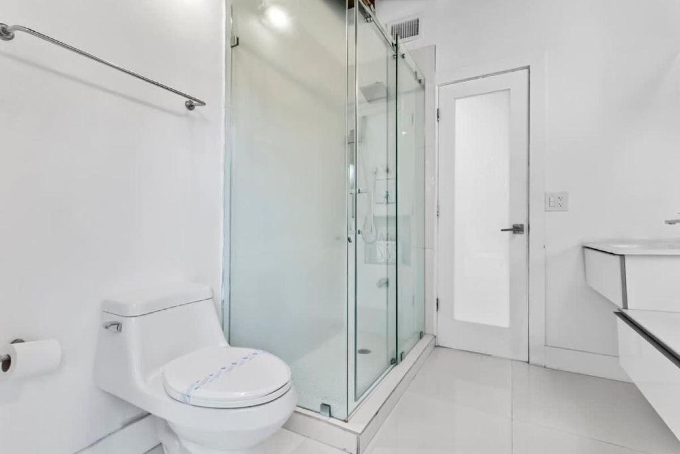 Casa de banho moderna com sanita, cabine de chuveiro em vidro e lavatório branco.