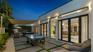 A modern outdoor patio with a ping pong table, a barbecue area, and a seating area with a sofa and cushions. - Luxury Miami Stay by Glam Homes (North Miami Beach)