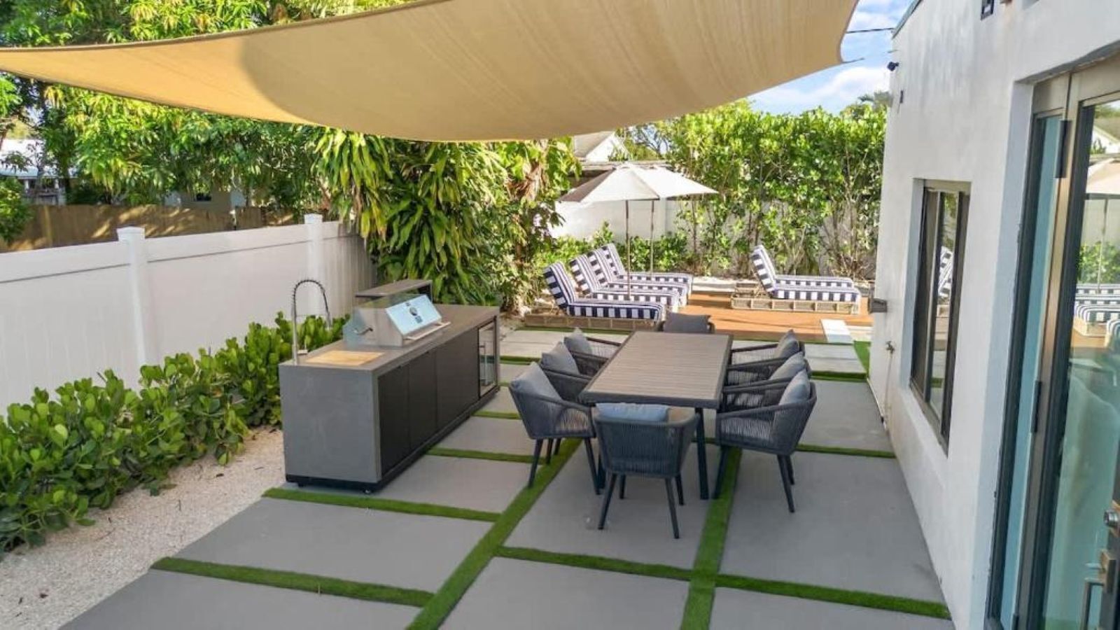 Une terrasse extérieure équipée d’un barbecue, de sièges et d’un espace ombragé.