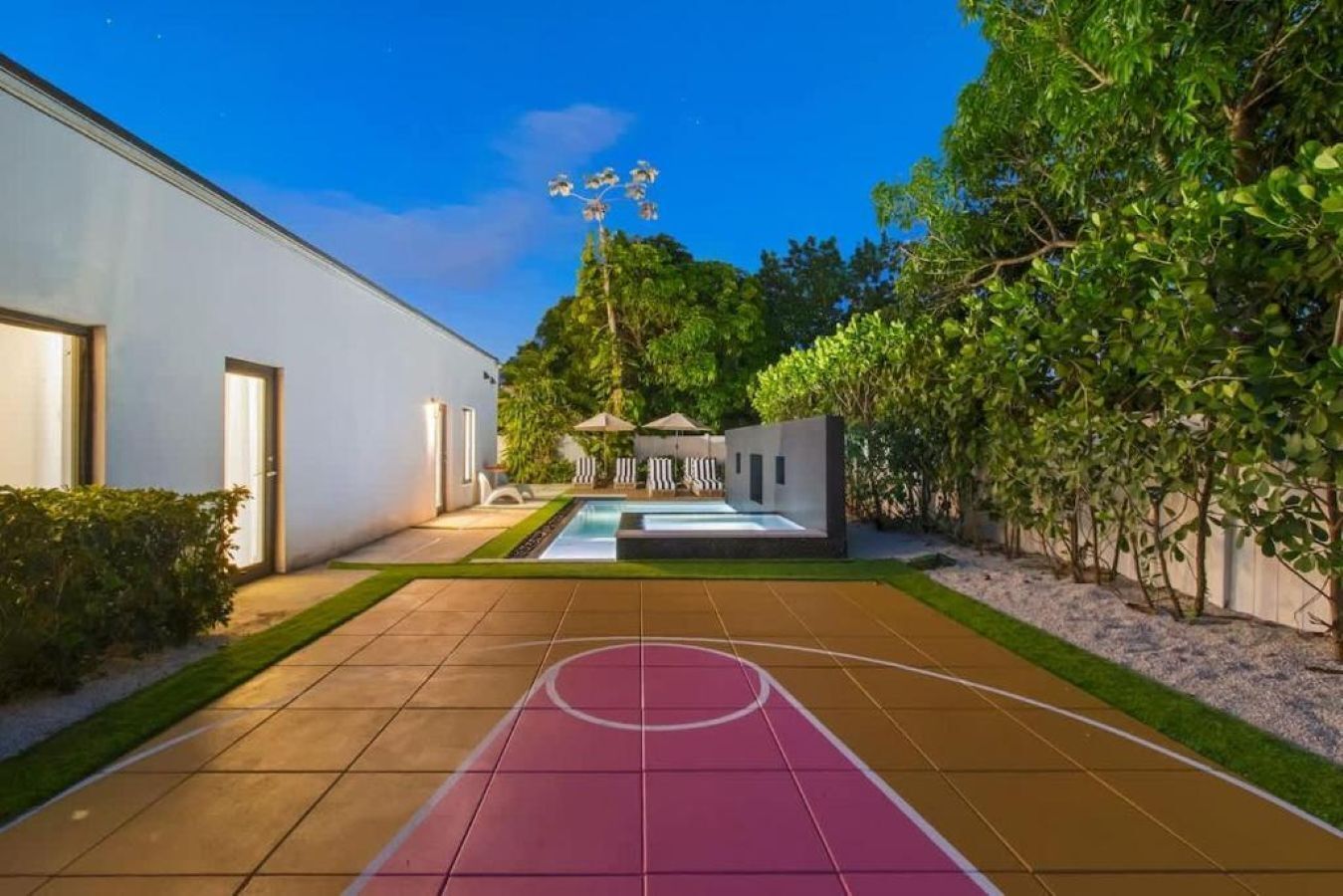 Uma quadra de basquete com piscina, cercada por um edifício moderno e vegetação.