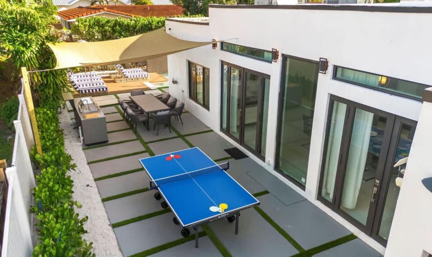 An outdoor ping pong table set up on a patio with a dining area and large windows.