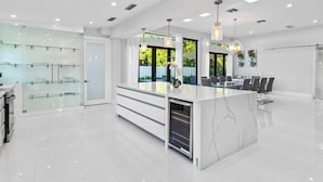 A modern kitchen with a central island, glass display cabinets, and a dining area with chairs. - Luxury Miami Stay by Glam Homes (North Miami Beach)