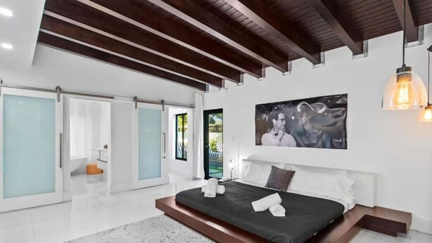 A modern bedroom with a large bed, a glass door leading to a balcony, and a painting on the wall. - Luxury Miami Stay by Glam Homes (North Miami Beach)