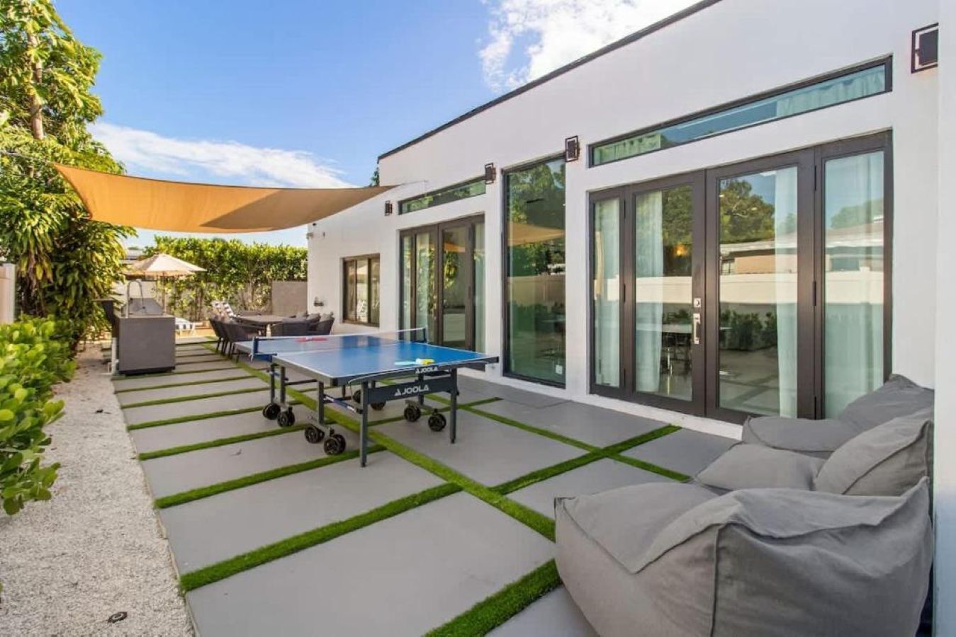 A modern outdoor patio with a ping pong table, outdoor seating, and a glass door entrance.