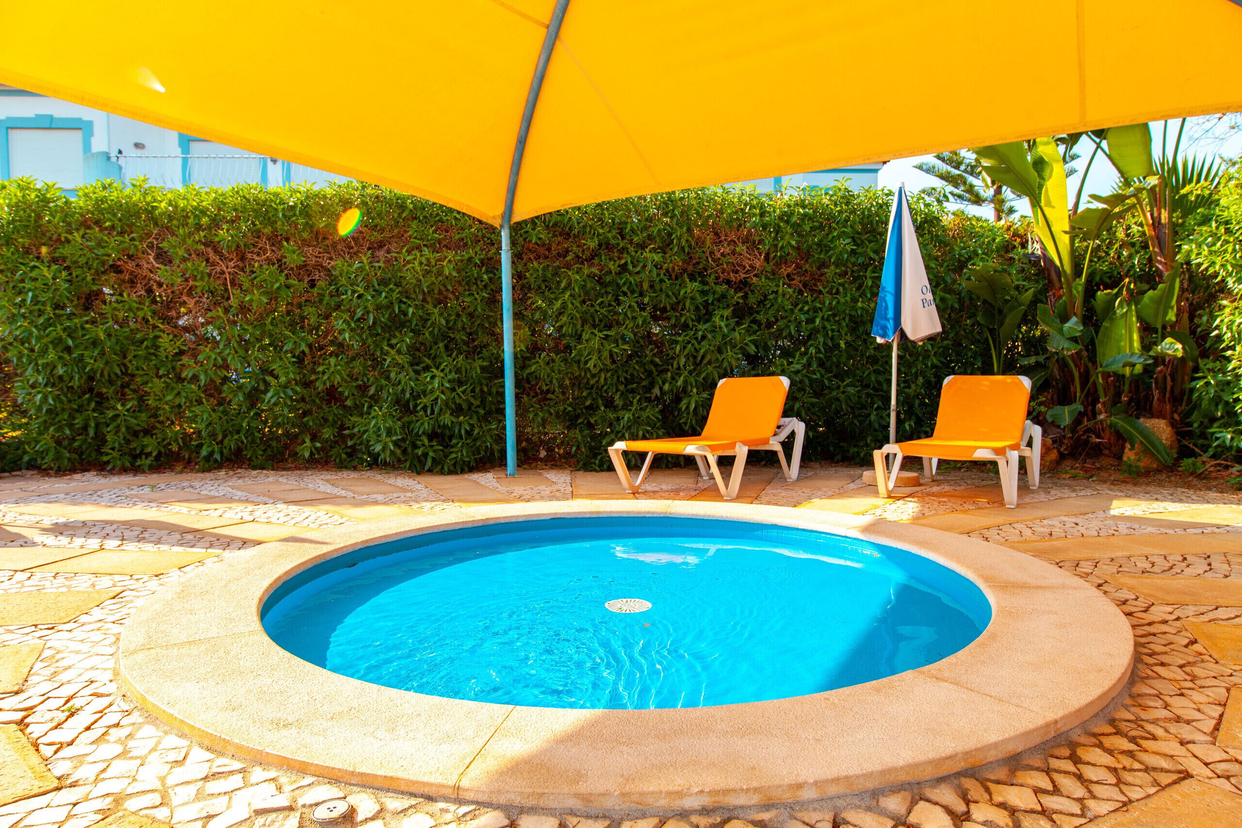 A swimming pool with two orange lounge chairs under a yellow umbrella.