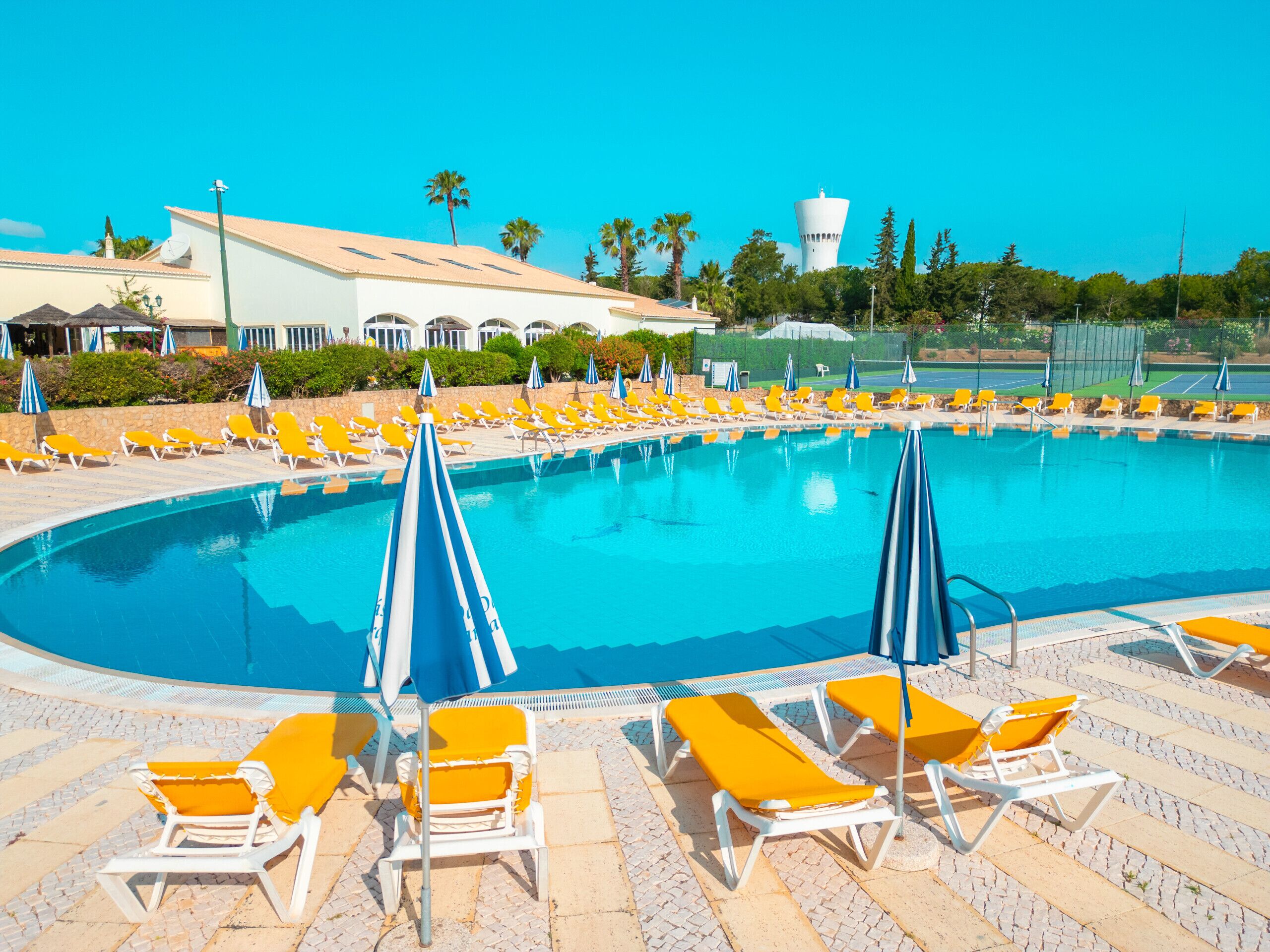 A large swimming pool with yellow lounge chairs and blue umbrellas.
