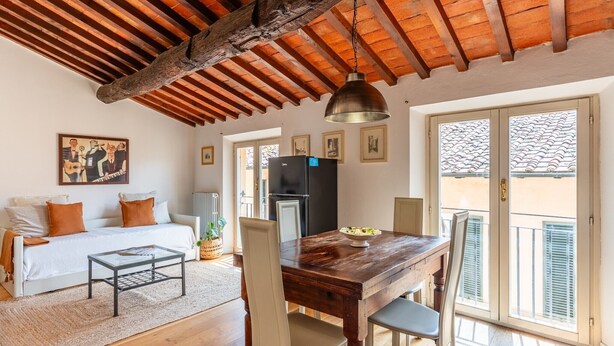 Una habitación acogedora con techo de madera, una mesa de comedor con sillas, un sofá con cojines, un refrigerador y una ventana con contraventanas.