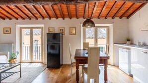 Una habitación con techo de madera, una mesa de comedor con sillas, un refrigerador negro y una zona de cocina con armarios blancos.