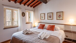 Un dormitorio con una cama grande, techo de madera, ventana con cortinas y tres cuadros con motivos florales en la pared.