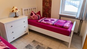 A bedroom with a bed, a nightstand, a lamp, a window with a view, and a radiator.