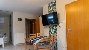 A dining area with a wooden table, chairs, a TV mounted on the wall, and a door.