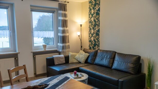 A living room with a black leather sofa, a wooden coffee table, a small side table, and a radiator.